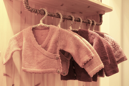 vestiti per bambini sistemati in un appendiabiti con grucce in corda