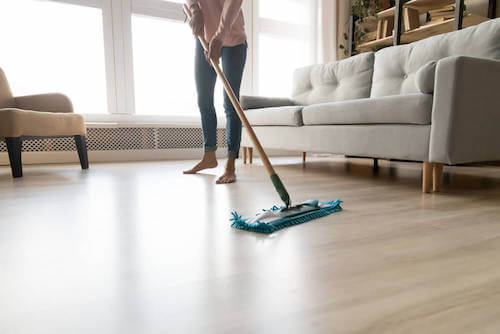 Donna che pulisce il pavimento il legno del salone.